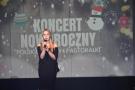 dziewczyna w czarnej sukience śpiewa w tle baner z napisem koncert noworoczny